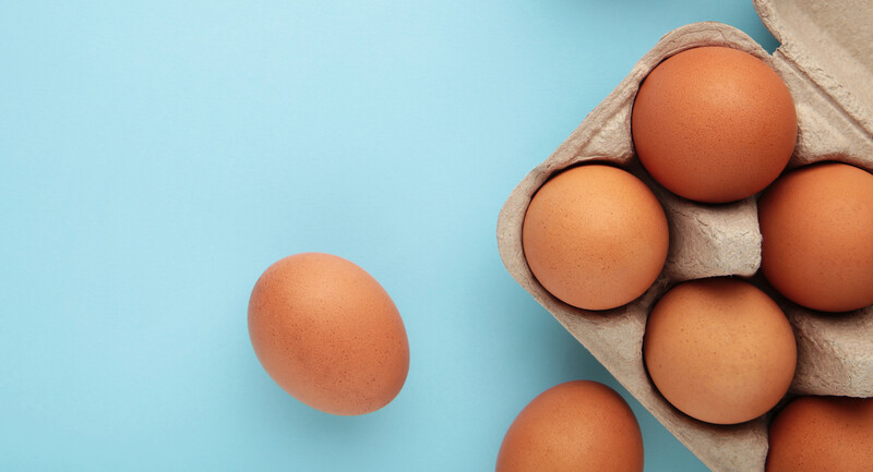 A carton of eggs on a blue background, with two eggs out to the side.