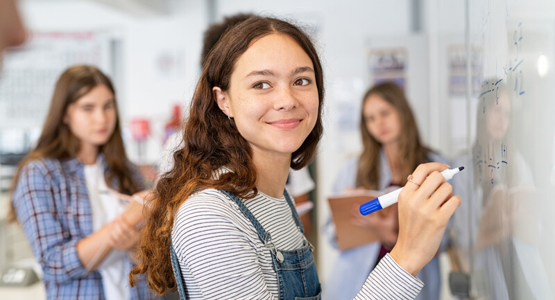 A smiling student solving a math equation on a whiteboard