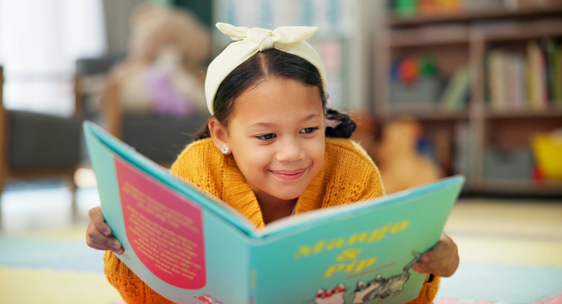 An elementary student smiling while reading a picture book