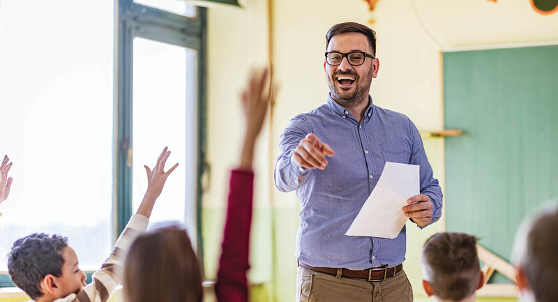 A happy teacher points to a classroom full of engaged, actively participating students 