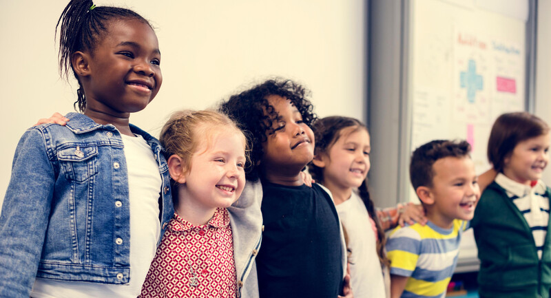 Elementary age children line up, hugging one another and smiling happily in a classroom