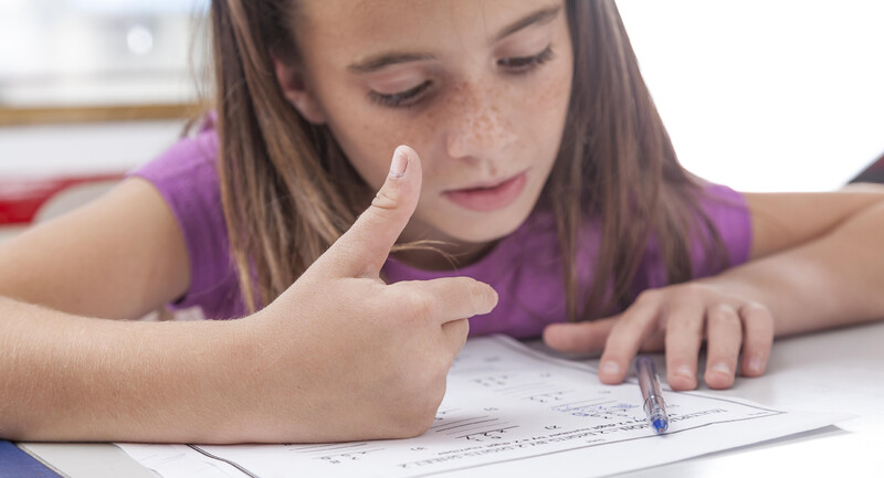 A student concentrating on a math worksheet and counting with her fingers