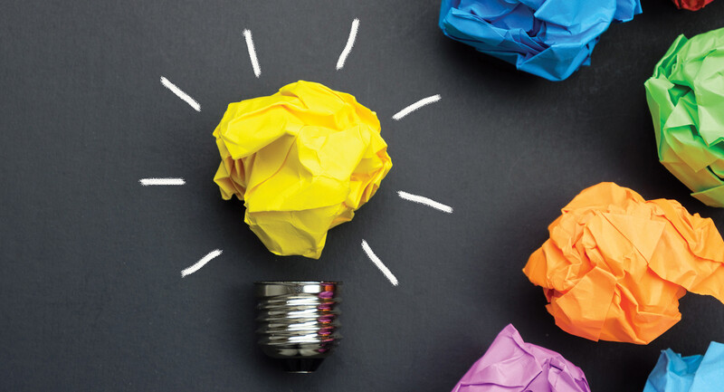 A series of crumpled balls of paper on a dark background, one of which looks like a lightbulb representing a good idea